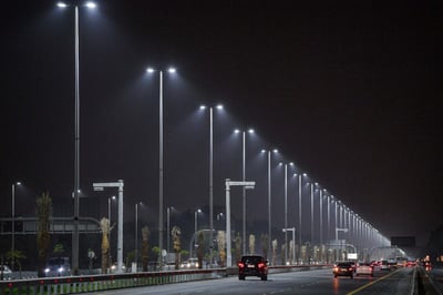 A night highway with smart street lighting and illuminated side lights, bustling with traffic.