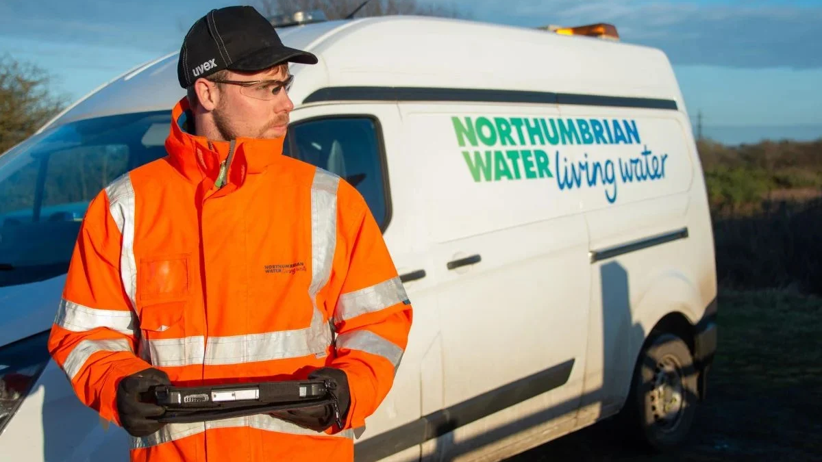 A utility worker in high-visibility gear holding a tablet in front of a branded Northumbrian Water service van.
