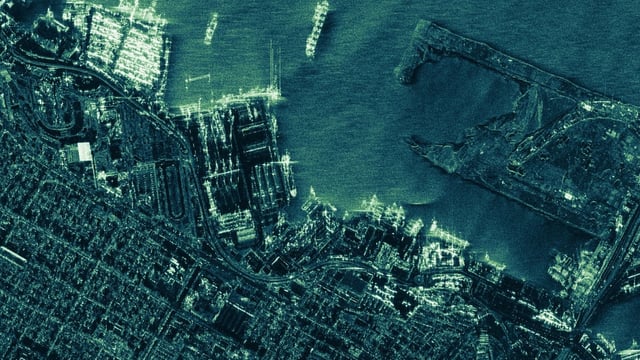 Green-toned ICEYE SAR satellite image showing a detailed aerial view of a coastal port city with ships and docks