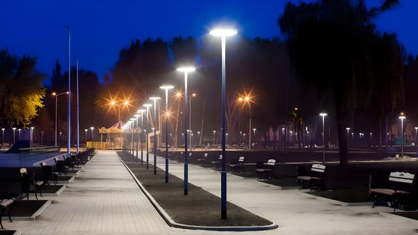 Row of illuminated LED street lamps lining a paved pedestrian walkway in a park at night.