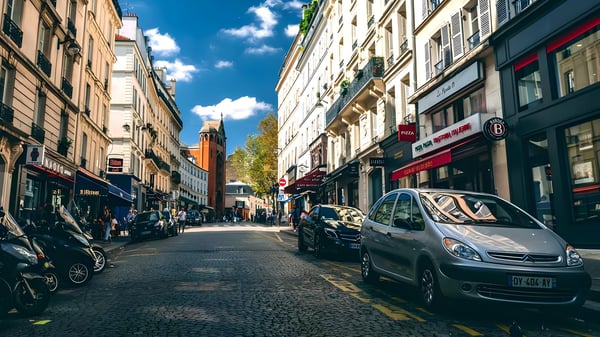 Cars and scooters parked along a narrow Parisian street lined with multi-story buildings and storefronts.
