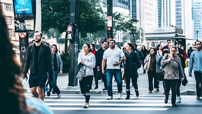 Pedestrians crossing a busy city street at a marked crosswalk surrounded by urban infrastructure and skyscrapers.