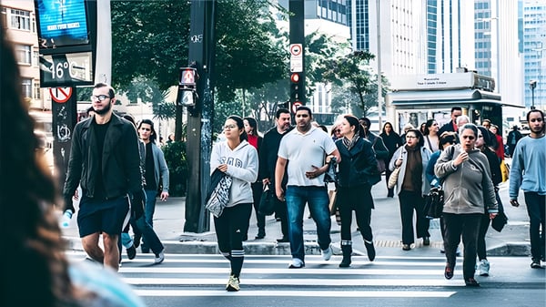 Pedestrians crossing a busy city street at a marked crosswalk surrounded by urban infrastructure and skyscrapers.