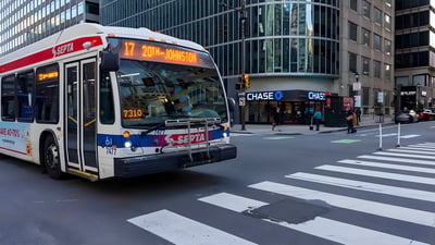 A SEPTA bus driving through a Philadelphia city intersection with a crosswalk and high-rise buildings.