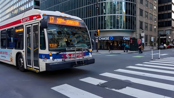 A SEPTA bus driving through a Philadelphia city intersection with a crosswalk and high-rise buildings.