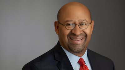 Headshot of former Philadelphia Mayor Michael Nutter wearing a suit, glasses, and a red tie against a gray background.