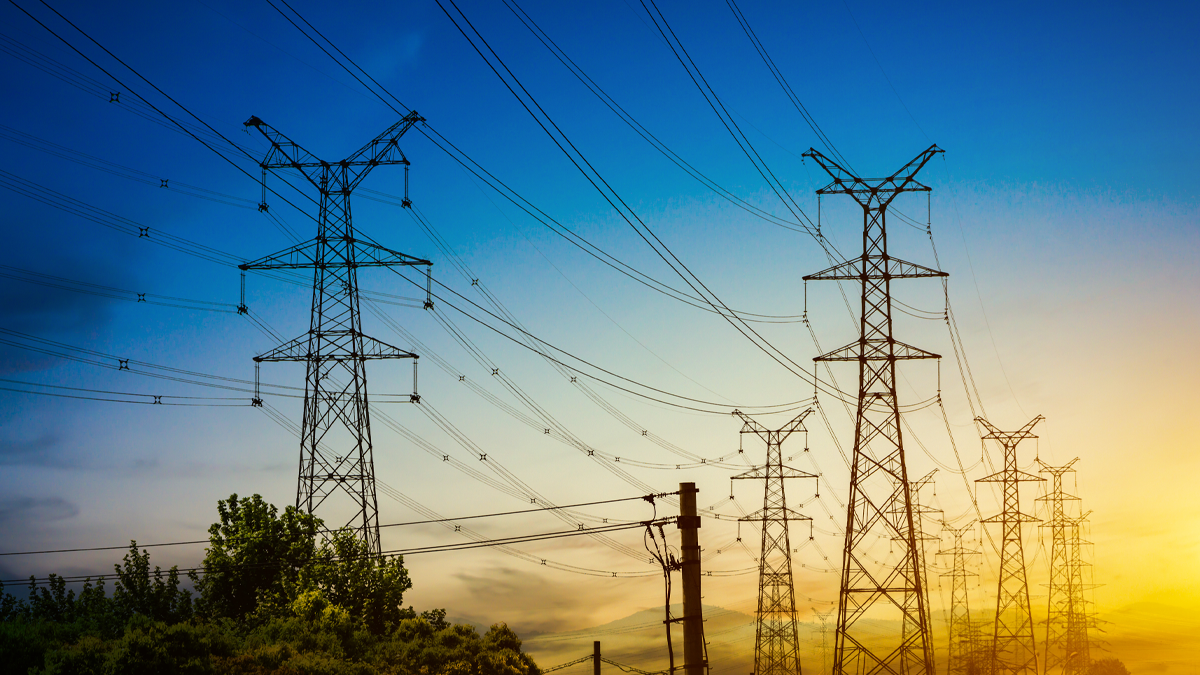 High-voltage power transmission towers and lines stretching across a landscape under a blue and yellow sunset sky