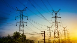High-voltage power transmission towers and lines stretching across a landscape under a blue and yellow sunset sky