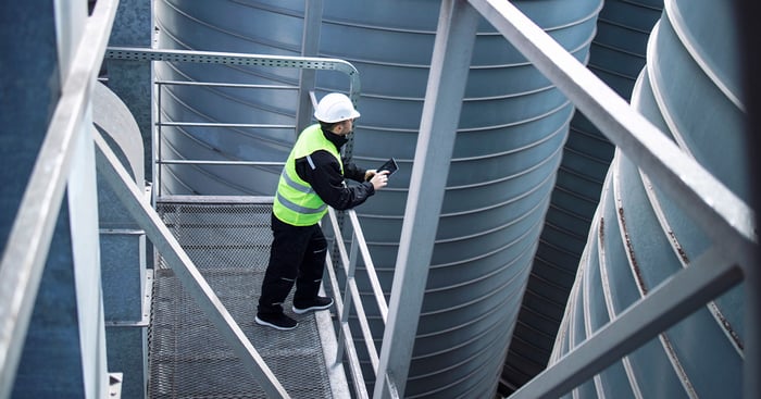 A utility employee using a digital device for remote tank monitoring in a water utility setting.