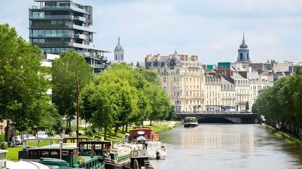 Houseboats moored on the Vilaine river in Rennes, France, with modern and historic architecture in the background.