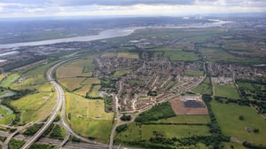 Aerial view of a South Essex town surrounded by green fields, highways, and the River Thames under a cloudy sky