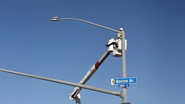 A bucket truck lift installs a Ubicquia smart streetlight sensor on a pole above a Boston Av. street sign.