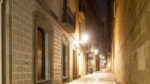 Wall-mounted streetlights illuminate a narrow stone alleyway between historic buildings at night.
