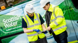Two Scottish Water workers in high-visibility vests and hard hats review a tablet in front of a branded utility van.