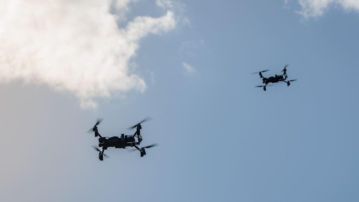 Two quadcopter drones flying in a blue sky with scattered white clouds