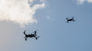 Two quadcopter drones flying in a blue sky with scattered white clouds
