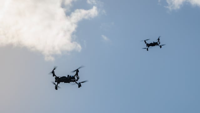 Two quadcopter drones flying in a blue sky with scattered white clouds