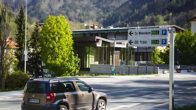 Digital parking guidance signs showing available spaces in a Slovenian city with a car driving past in the foreground.