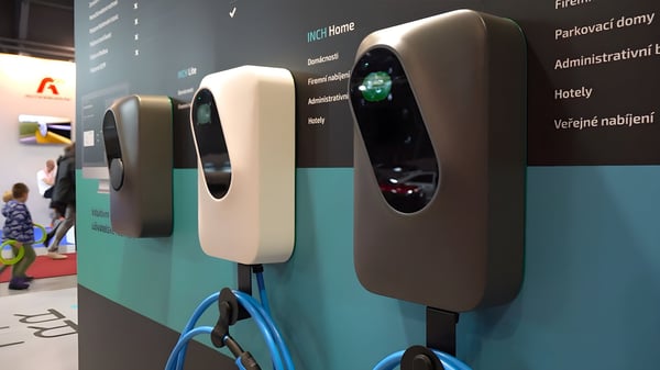 Three wall-mounted EV charging stations with blue cables displayed on a branded exhibition booth wall.
