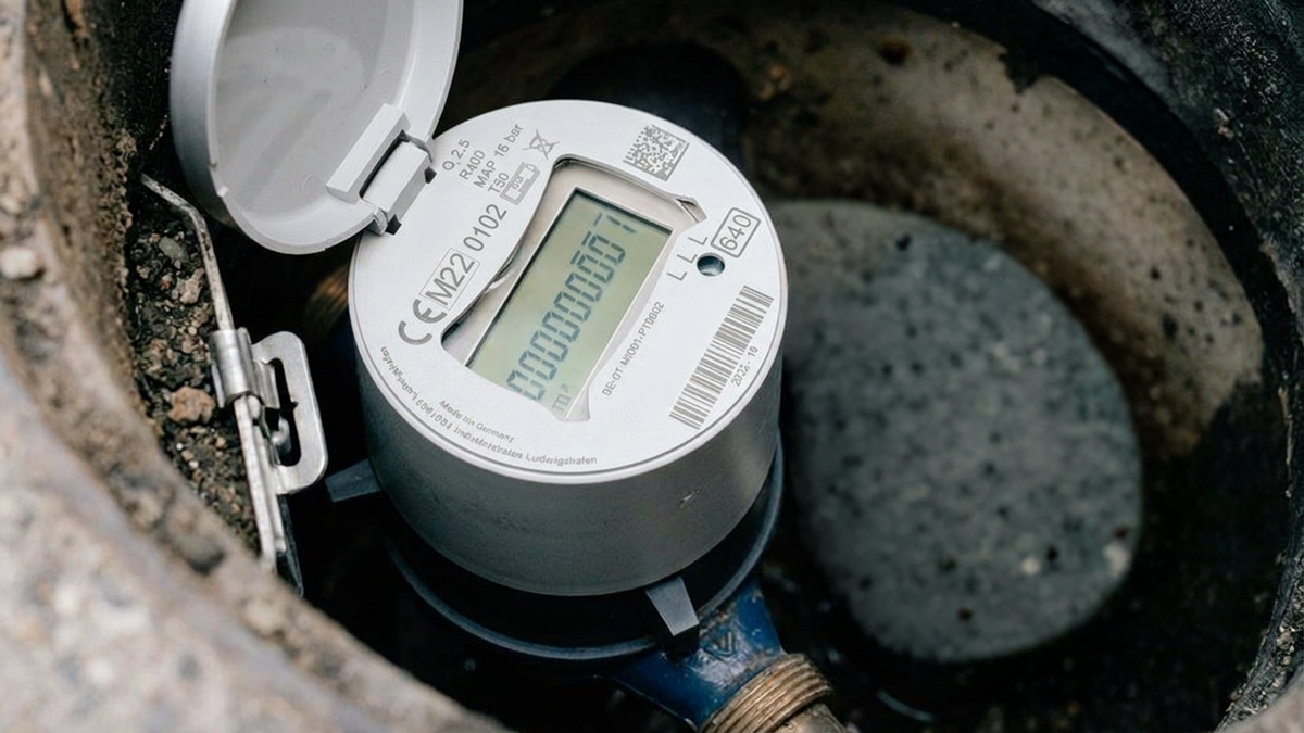A digital smart water meter with an open protective lid installed inside an underground utility pit.