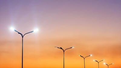 Row of illuminated double-arm LED street lights against a purple and orange sunset sky.