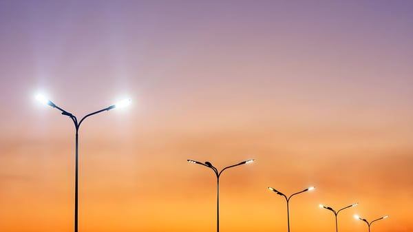 Row of illuminated double-arm LED street lights against a purple and orange sunset sky.