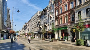 Pedestrians walking along a paved street lined with historic buildings, storefronts, and streetlights in Katowice, Poland