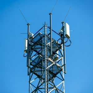 Low-angle view of a metal telecommunications tower with antennas and transmitters against a clear blue sky