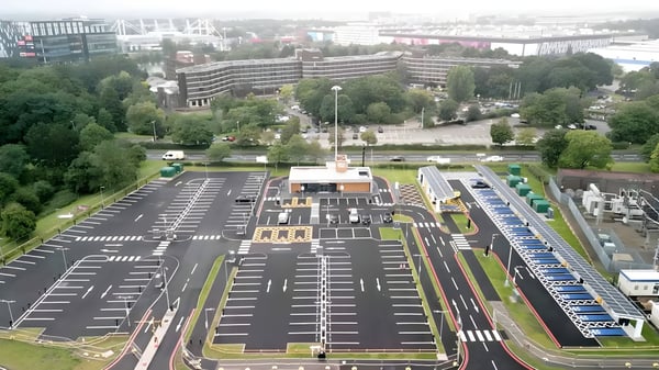 Aerial view of a large electric vehicle charging hub with solar canopies, parking bays, and a central service building.