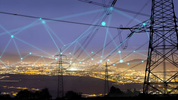 High-voltage power lines and transmission towers over a city at night with a blue digital network overlay.