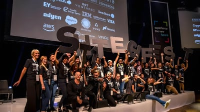 A group on stage holding large STHLM TECH FEST letters in front of a screen displaying AWS, IBM, and Salesforce logos.