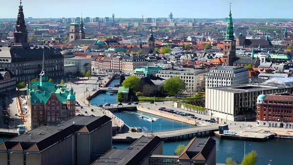 High-angle cityscape of Copenhagen featuring historic spires, the Slotsholmen canal, and modern urban infrastructure.