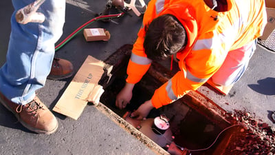 A utility worker in a high-visibility orange jacket installs a smart water meter inside an underground street vault.