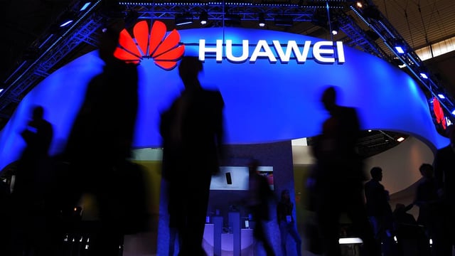 People shadow in front of a huwawei logo at a smart city exhibition.