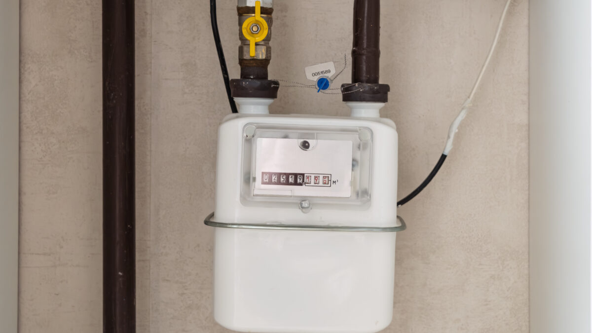 Close-up of a white residential gas meter with a digital display, connected to brown pipes and a yellow valve.