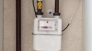 Close-up of a white residential gas meter with a digital display, connected to brown pipes and a yellow valve.