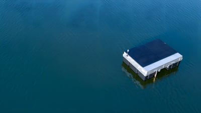 Aerial drone view of a solar-powered LG Sonic MPC-Buoy floating on a body of water for algae control.