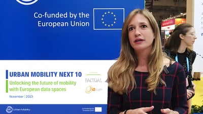 A woman speaking in front of an Urban Mobility Next 10 banner co-funded by the European Union at a conference.