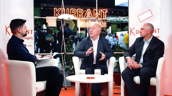 Three men in suits sit in white armchairs for a panel discussion at a Kurrant Insights branded event booth.