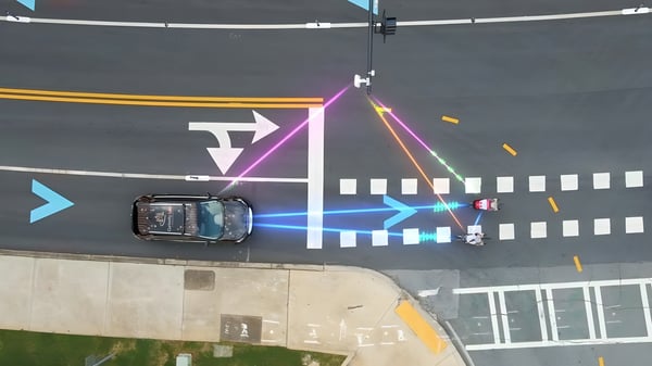 Aerial view of a car approaching a crosswalk with digital light overlays connecting the vehicle, pedestrians, and sensors.