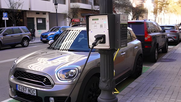 Electric vehicle charging from a lamppost-mounted power box on a city street in Valencia, Spain.