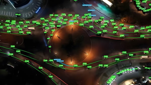 Aerial night view of a traffic roundabout with green digital bounding boxes and motion paths tracking vehicles.