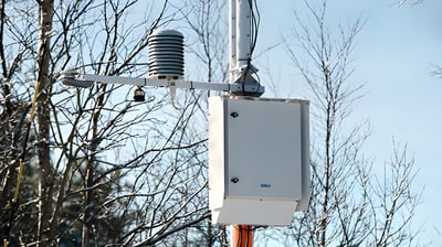 Road weather information system station with a multi-plate radiation shield and control box mounted on a utility pole.