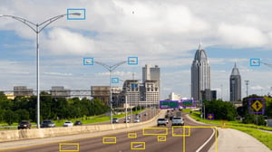 AI object detection boxes overlaying a highway with traffic, streetlights, and a city skyline in the background