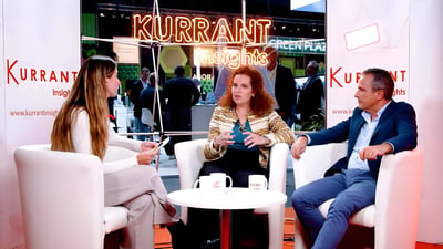 Three people sit in white armchairs for a panel discussion at a Kurrant Insights event booth.