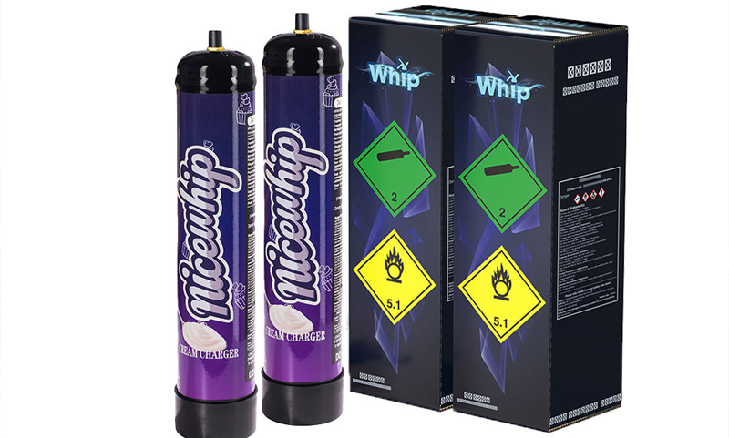 Two purple Nicewhip nitrous oxide cream charger canisters standing next to two black Whip branded cardboard boxes