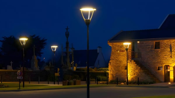 Illuminated modern LED street lamps along a paved road and stone building at night.