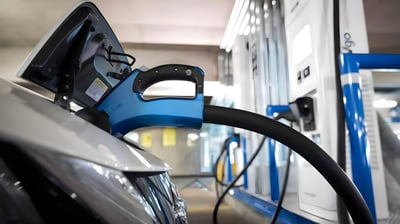 A blue CHAdeMO connector plugged into a white electric vehicle at an EVgo charging station in a parking garage.