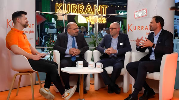 Four men in business attire sit in white armchairs for a Kurrant Insights panel discussion on a stage with orange flooring.