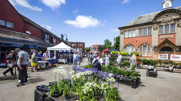 Pedestrians and market stalls in a brick-paved square outside the historic Wrexham General Market building.